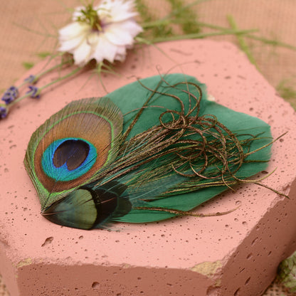 Green peacock feather hair clip on a pink stone with flowers and greenery