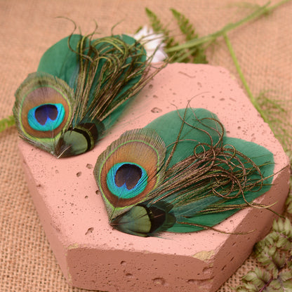 Green peacock feather hair clips on a pink stone with flowers and greenery