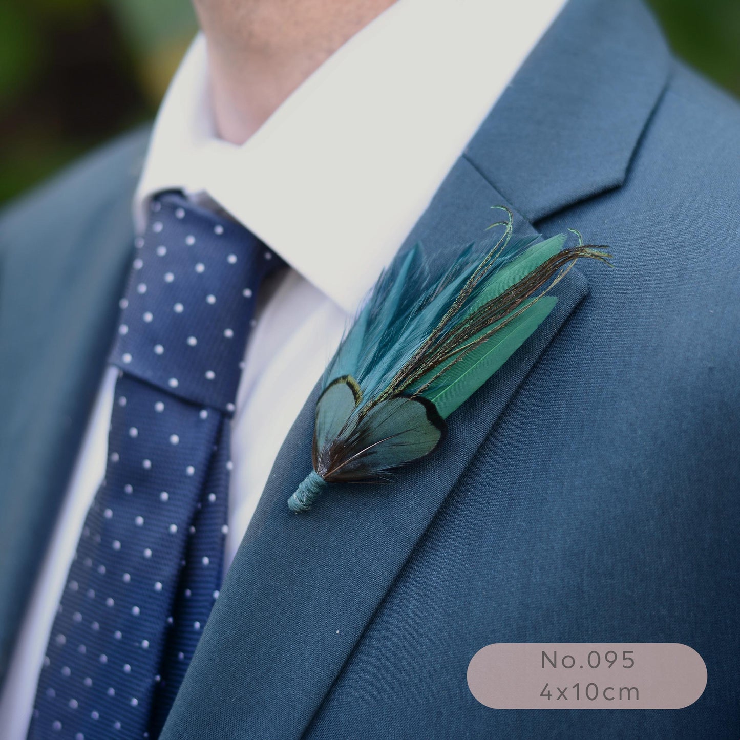 A close-up of a men's formal wear featuring a slate blue suit jacket, a blue polka-dot tie, and a teal and green feather boutonniere on the lapel.