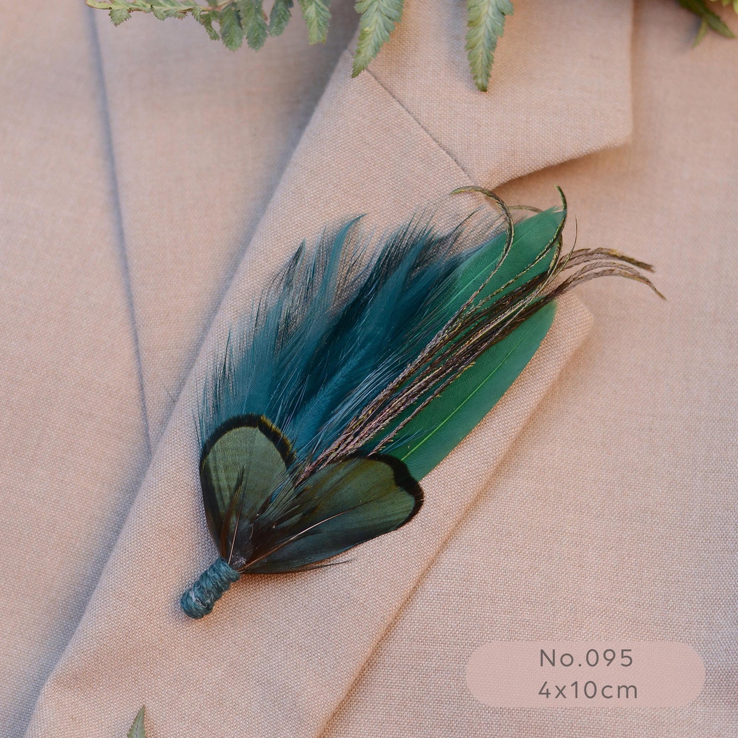 A decorative feather brooch with teal, green, and black feathers, pinned to a beige blazer. 