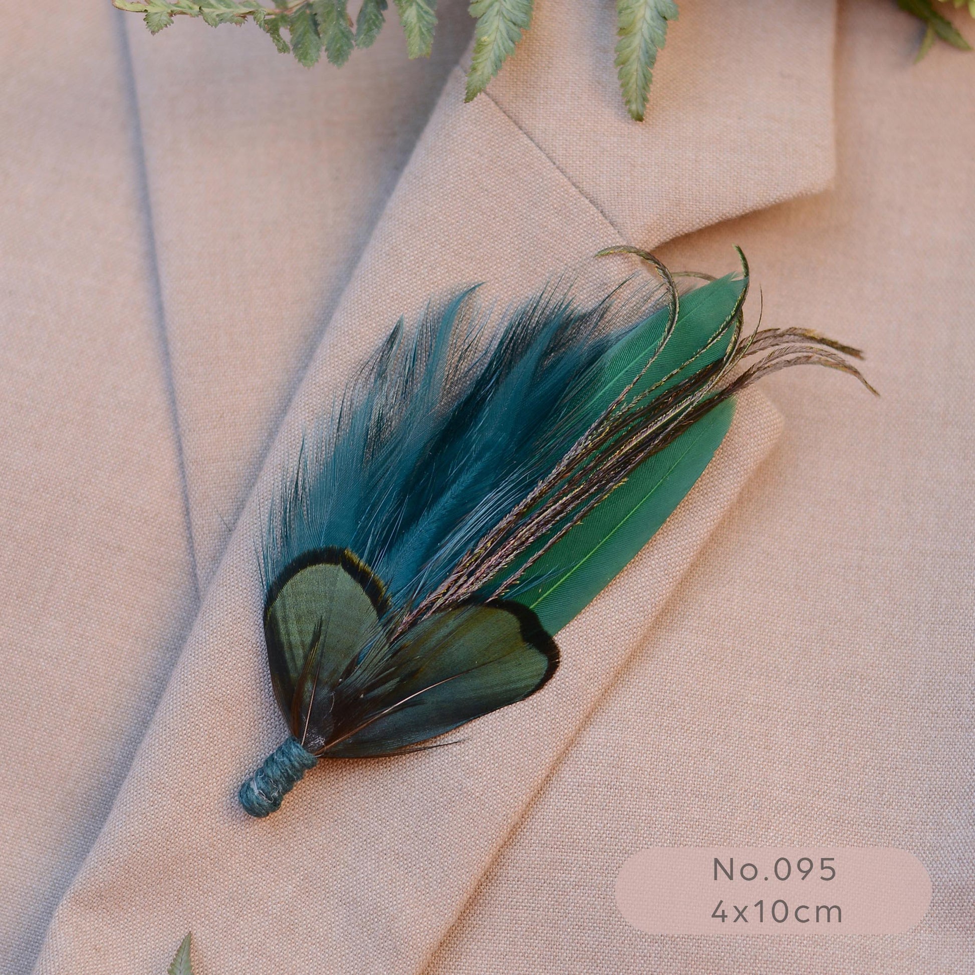 A decorative feather brooch with teal, green, and black feathers, pinned to a beige blazer. 