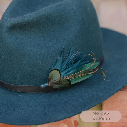 A close-up of a dark teal felt hat with a decorative feather hat pin  in teal and green.