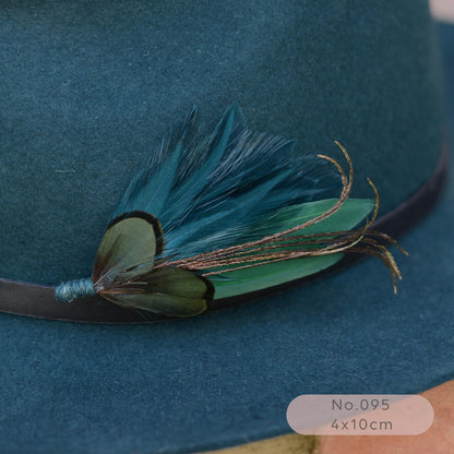A close-up of a dark teal felt hat with a decorative feather hat pin  in teal and green.