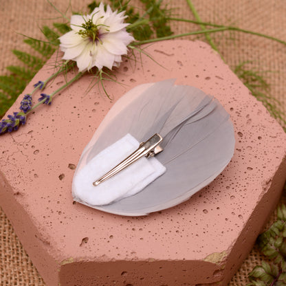 Hexagonal pink stone wih  a feather hair clip in grey and blush pink upside down to show a crocodile style clip attachment with flowers and leaves.