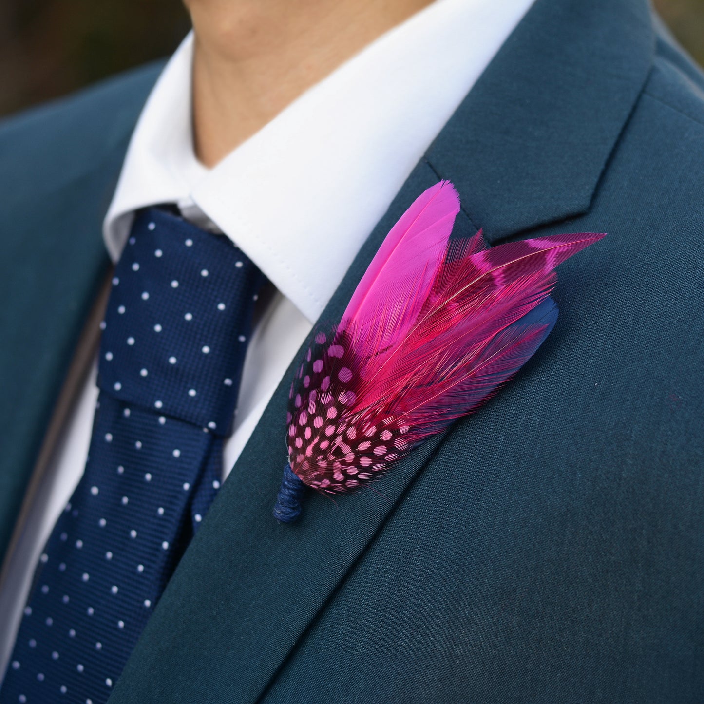 A man wearing a formal suit in dark blue with a feather buttonhole in hot pink and navy blue