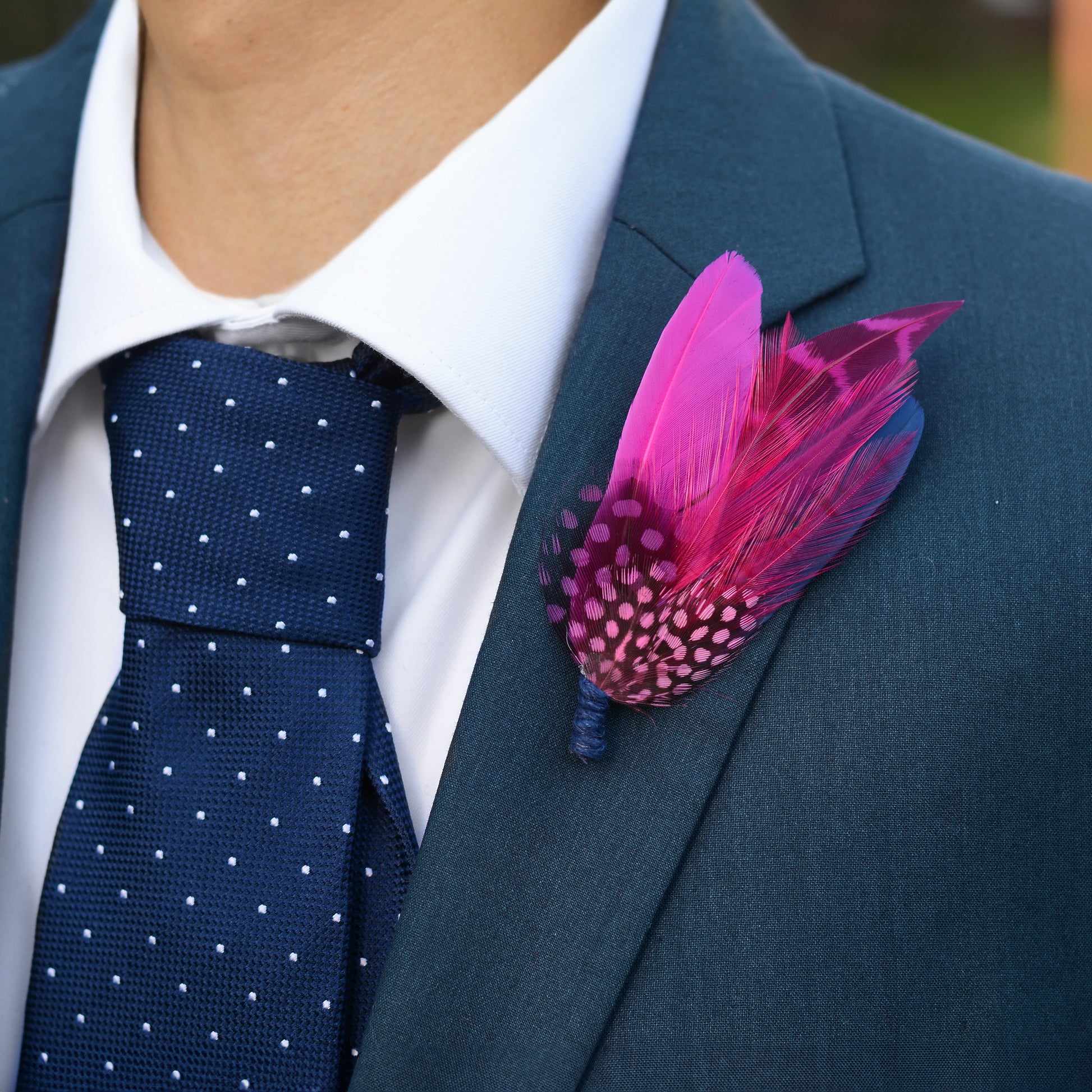 A man wearing a formal suit in dark blue with a feather buttonhole in hot pink and navy blue