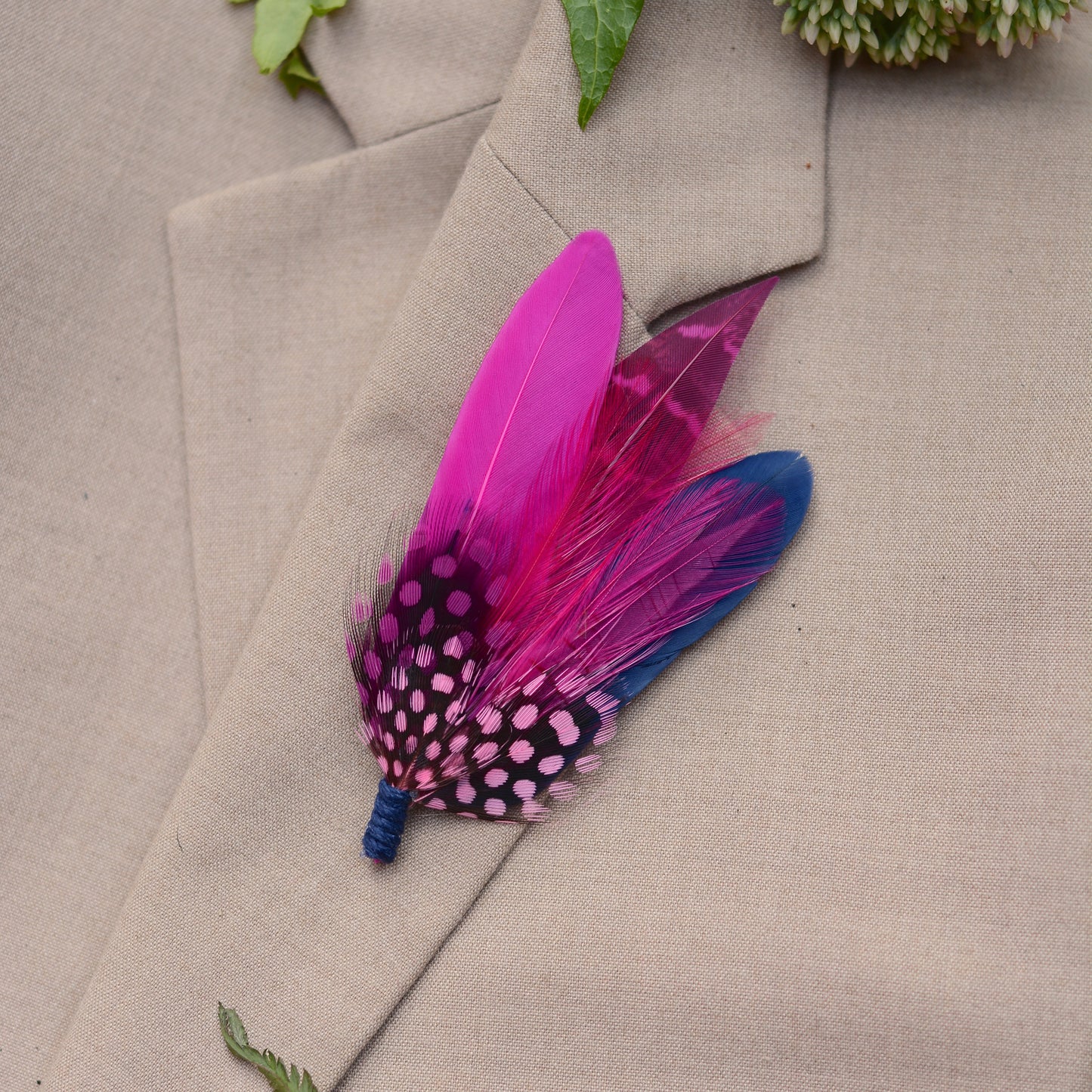 Feather boutonniere in hot pink and navy blue on a beige suit lapel.
