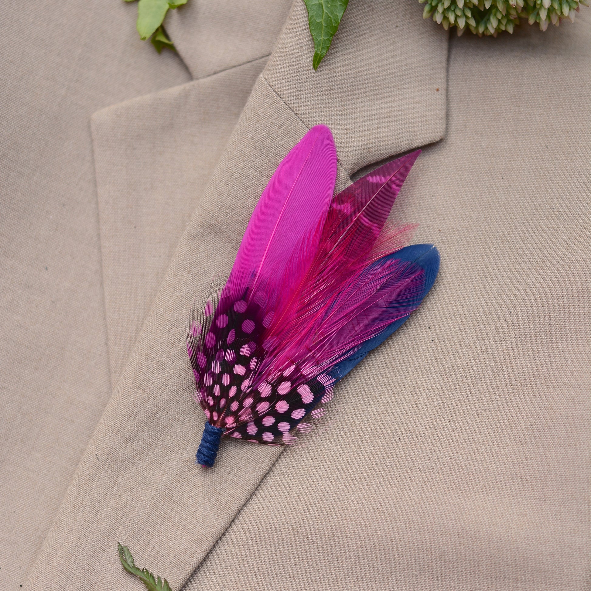 Feather boutonniere in hot pink and navy blue on a beige suit lapel.