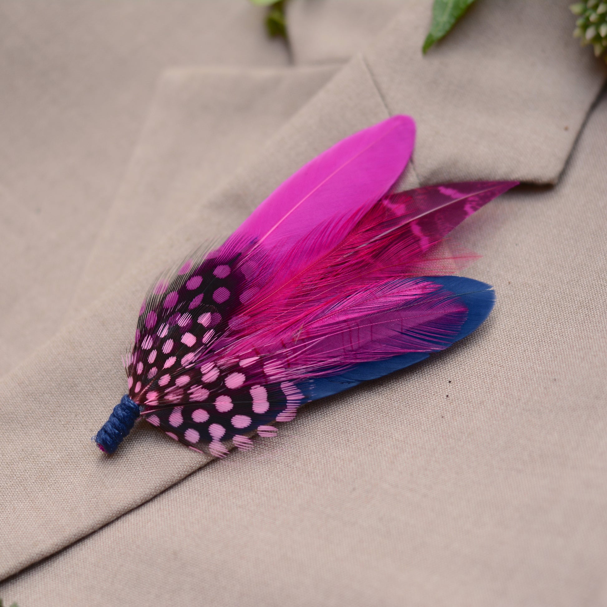 Feather lapel pin in hot pink and navy blue on a beige suit lapel.