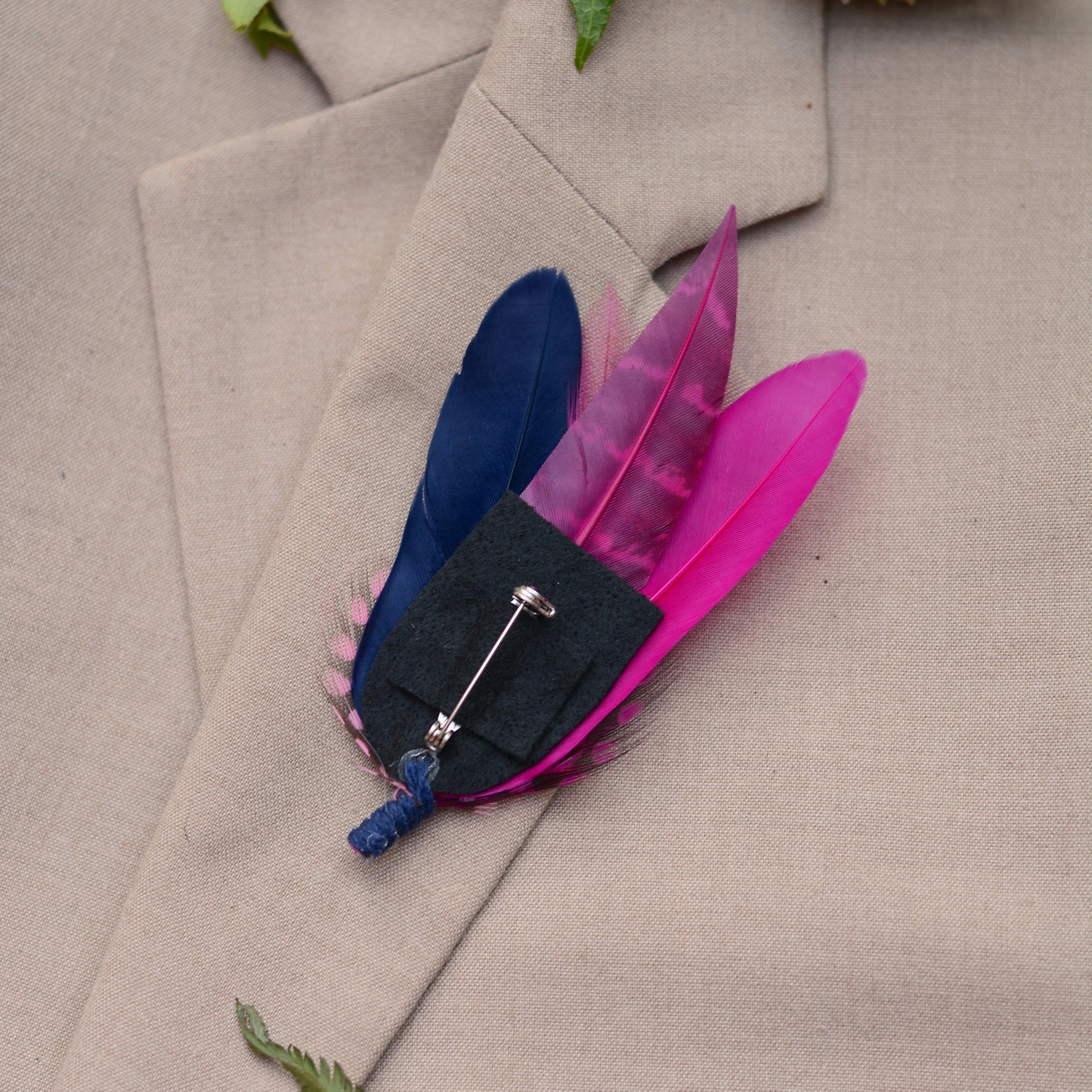 Feather brooch in hot pink and navy blue on a beige suit lapel, upside down tio show felt bakc and roll lock clasp