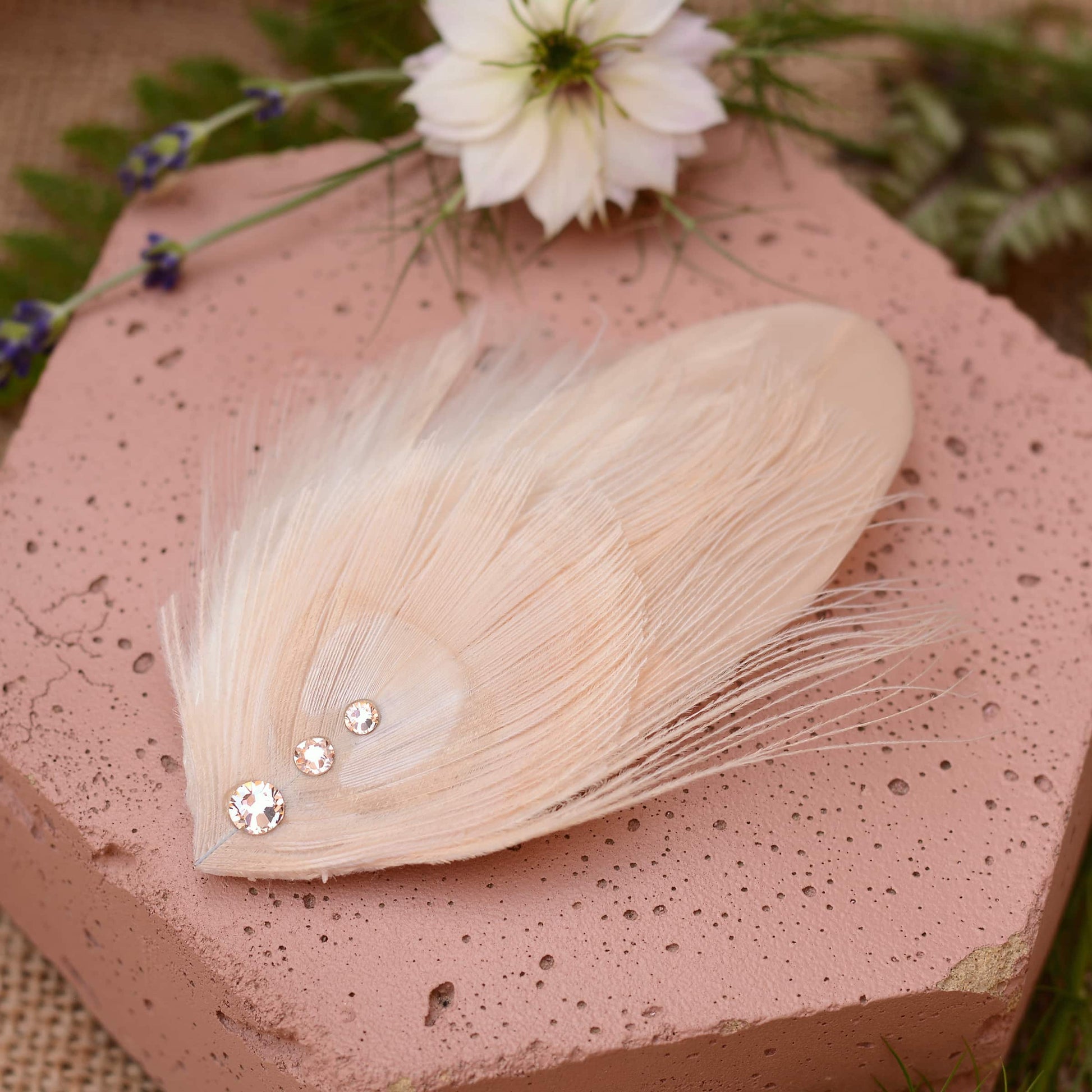 ivory and blush pink peacock Feather hair clip with crystals on a pink stone with flowers in the background