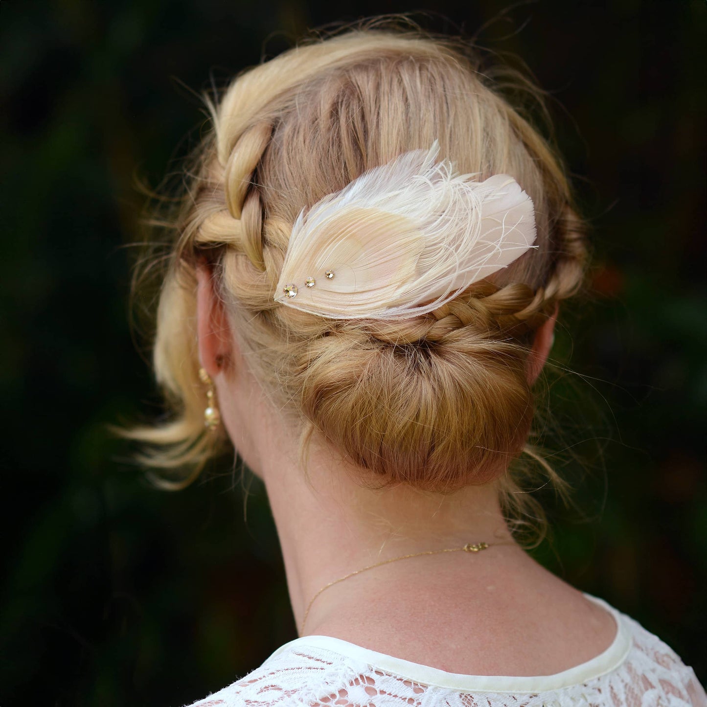 Person with braided hair with a decorative ivory and blush pink peacock Feather hair clip feather hairpiece  with crystals against a dark background