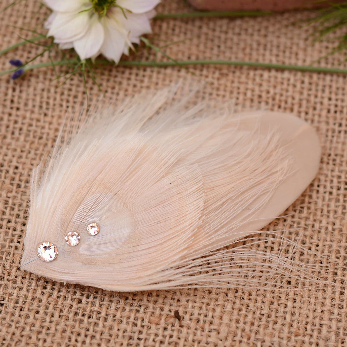 ivory and blush pink peacock Feather hair clip with crystals on burlap fabric with flowers in the background