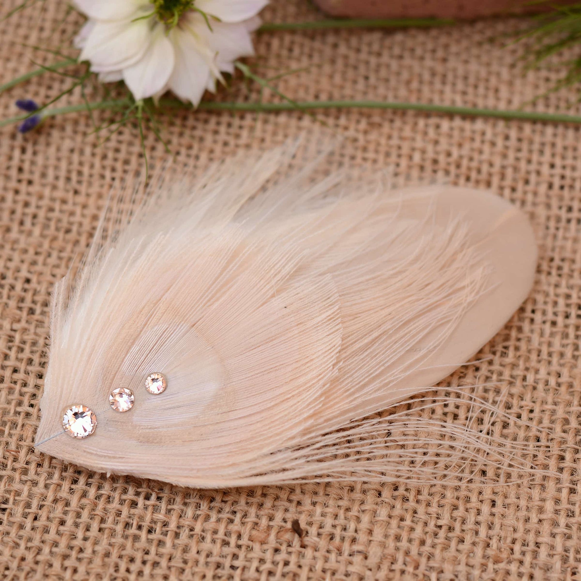 ivory and blush pink peacock Feather hair clip with crystals on burlap fabric with flowers in the background