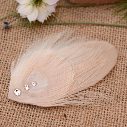 ivory and blush pink peacock Feather hair clip with crystals on burlap fabric with flowers in the background