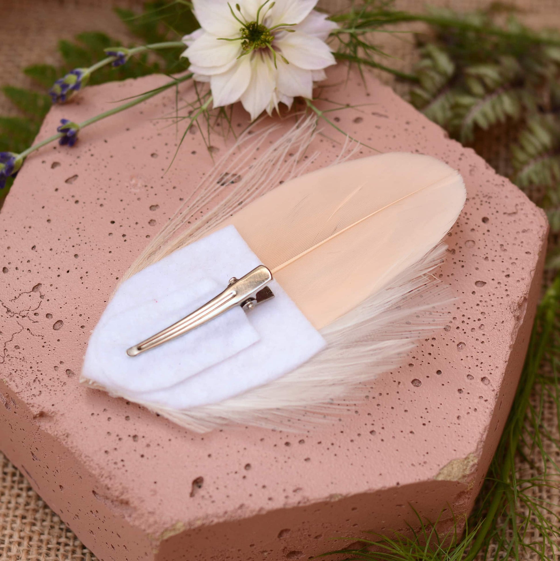 ivory and blush pink peacock Feather hair clip with crystals on a pink stone with flowers in the background