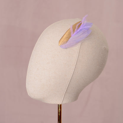 small feather hair clip in pastel lavender purple and gold with different texture feathers on the side of a canvas mannequin head