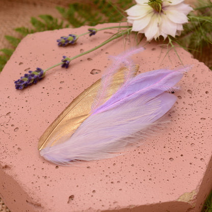 small feather hair clip in pastel lavender purple and gold with different texture feathers on a pink stone with flowers