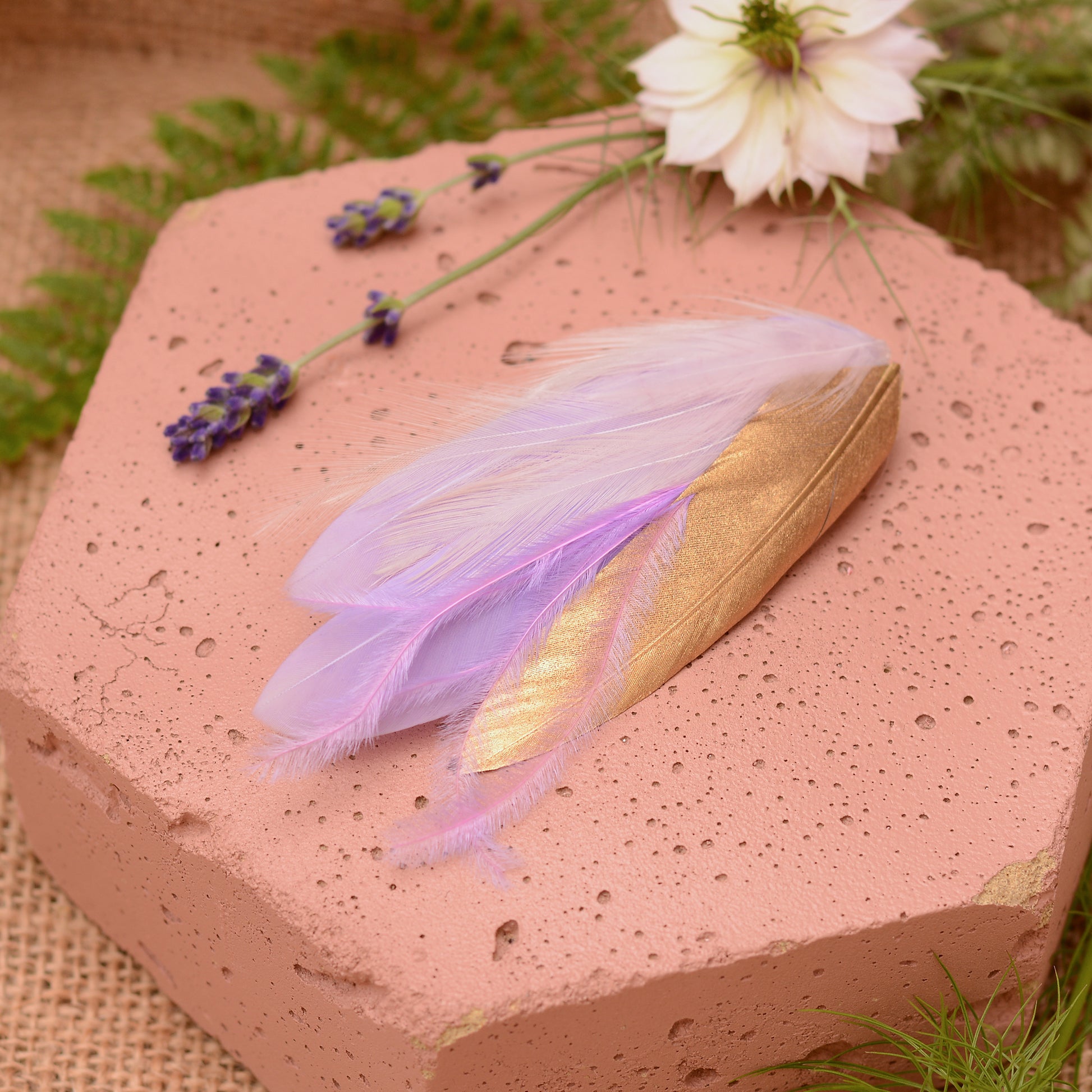 small feather hair clip in pastel lavender purple and gold with different texture feathers on a pink stone with flowers