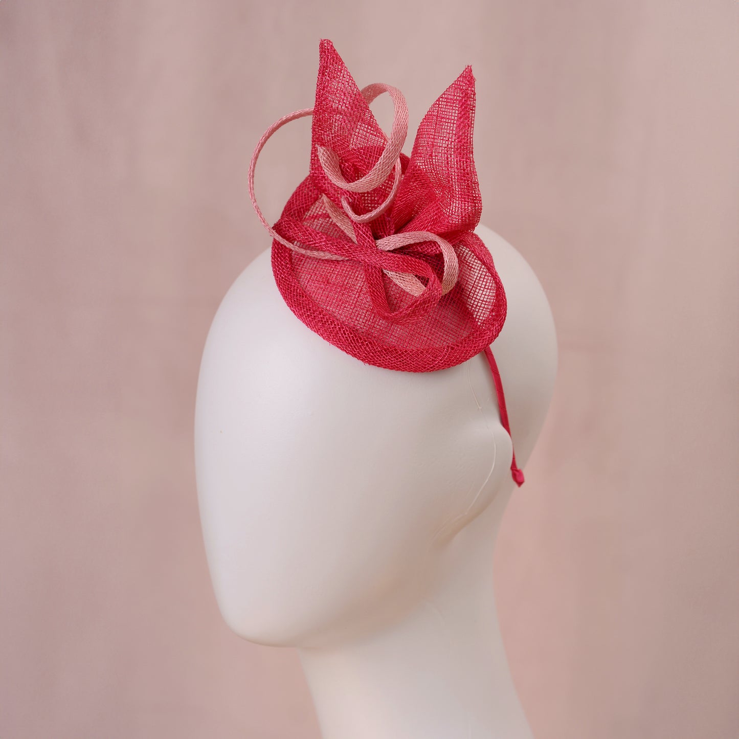 A pink sinamay side perching fascinator in two shades of tonal pink displayed on a white mannequin head against a soft pink background.