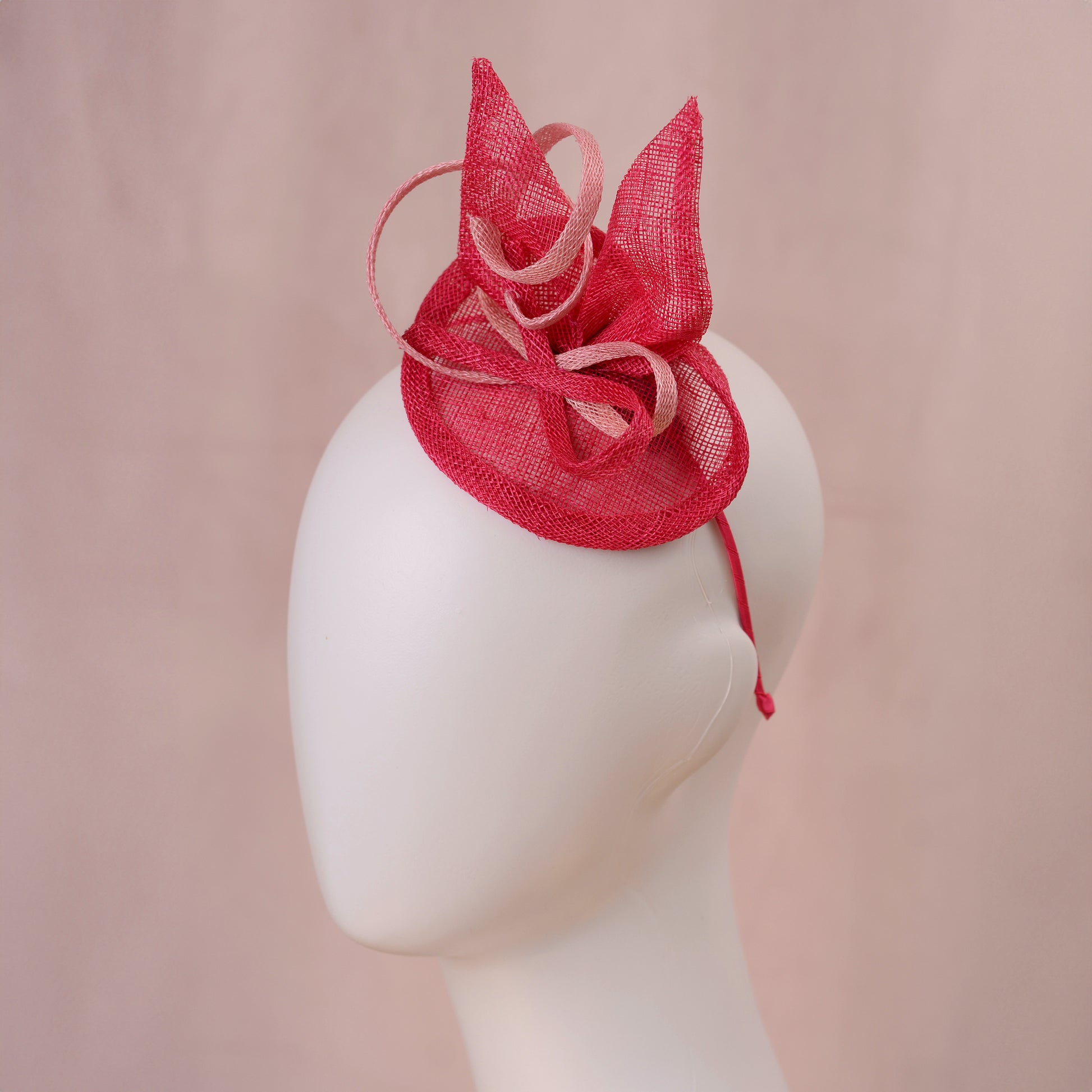 A pink sinamay side perching fascinator in two shades of tonal pink displayed on a white mannequin head against a soft pink background.