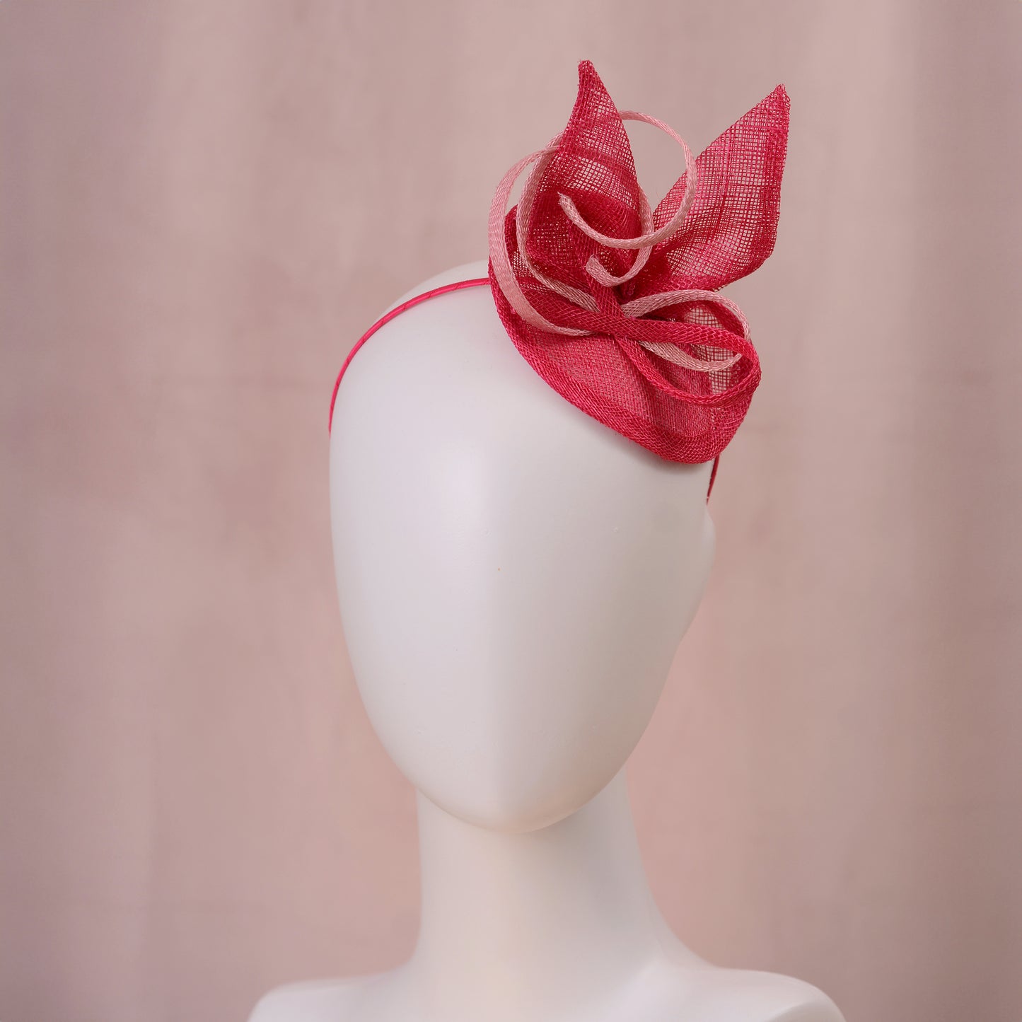 A pink sinamay side perching fascinator in two shades of tonal pink displayed on a white mannequin head against a soft pink background.