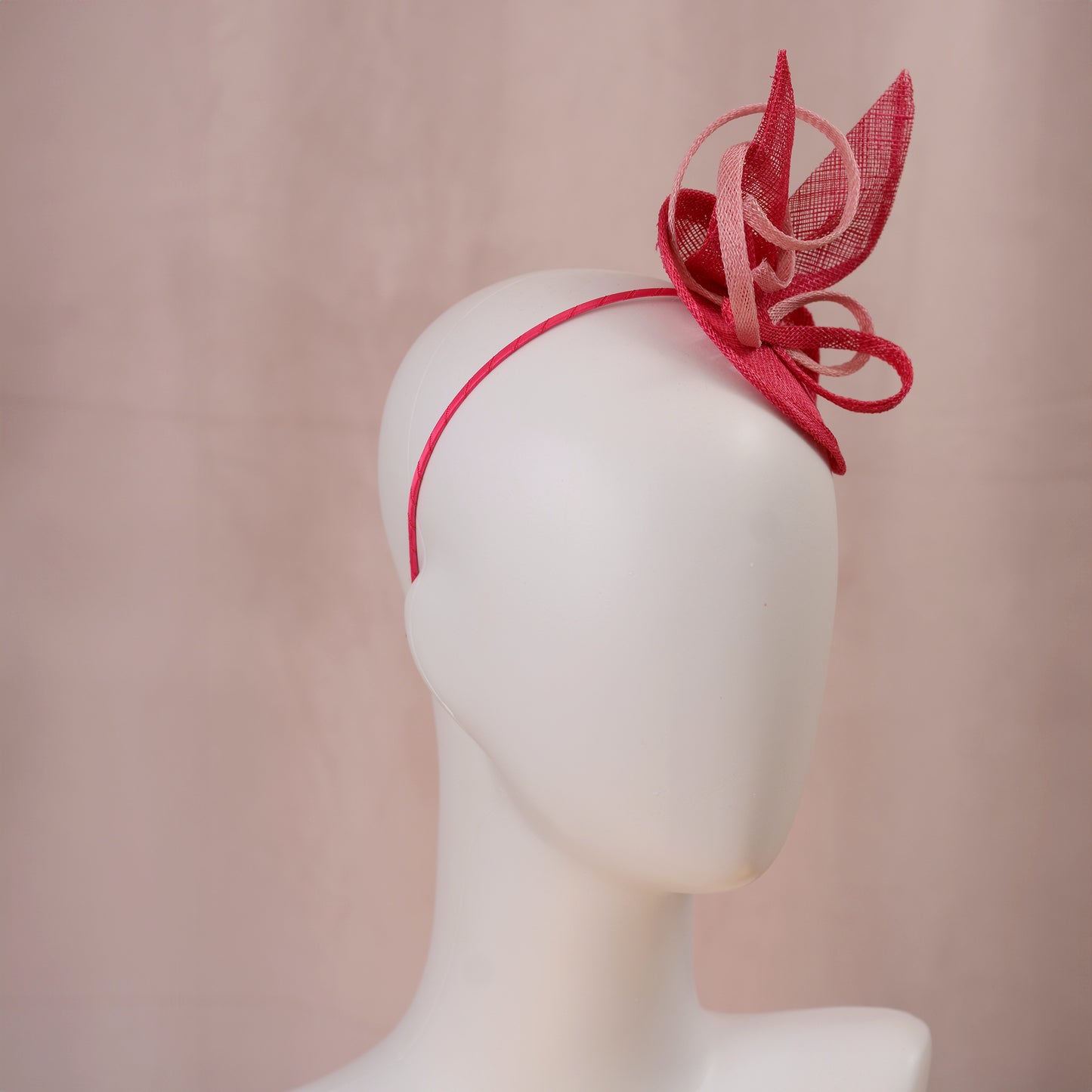 A pink sinamay side perching fascinator in two shades of tonal pink displayed on a white mannequin head against a soft pink background.
