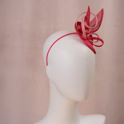 A pink sinamay side perching fascinator in two shades of tonal pink displayed on a white mannequin head against a soft pink background.
