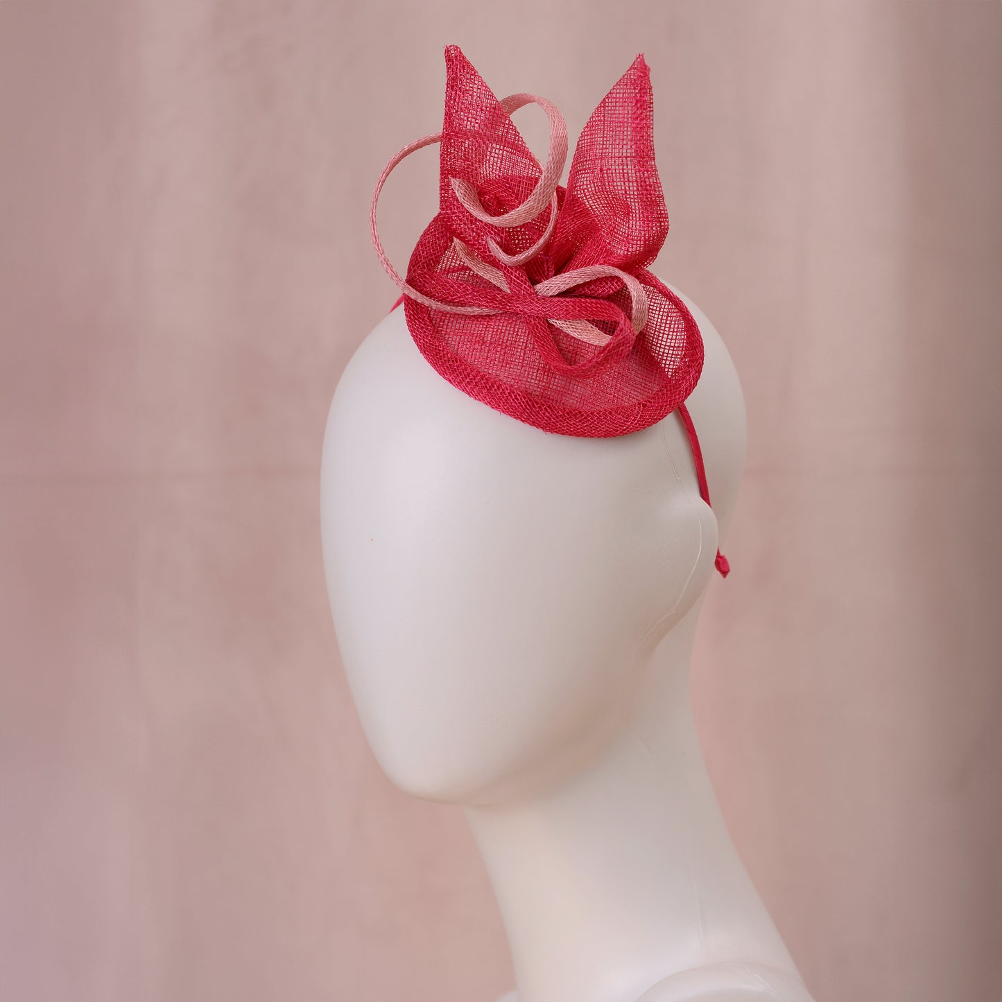 A pink sinamay side perching fascinator in two shades of tonal pink displayed on a white mannequin head against a soft pink background.