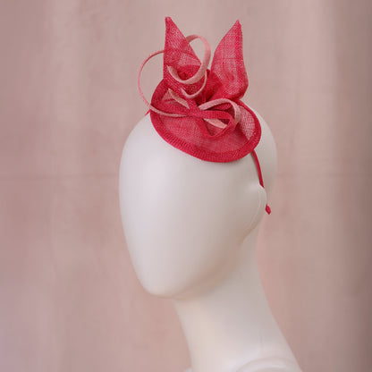 A pink sinamay side perching fascinator in two shades of tonal pink displayed on a white mannequin head against a soft pink background.