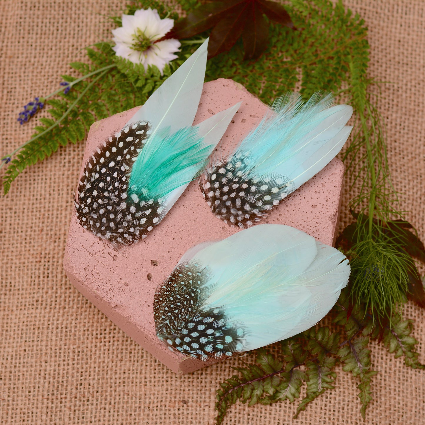 Mint green feather hair clips on a pink stone with flowers and plants around