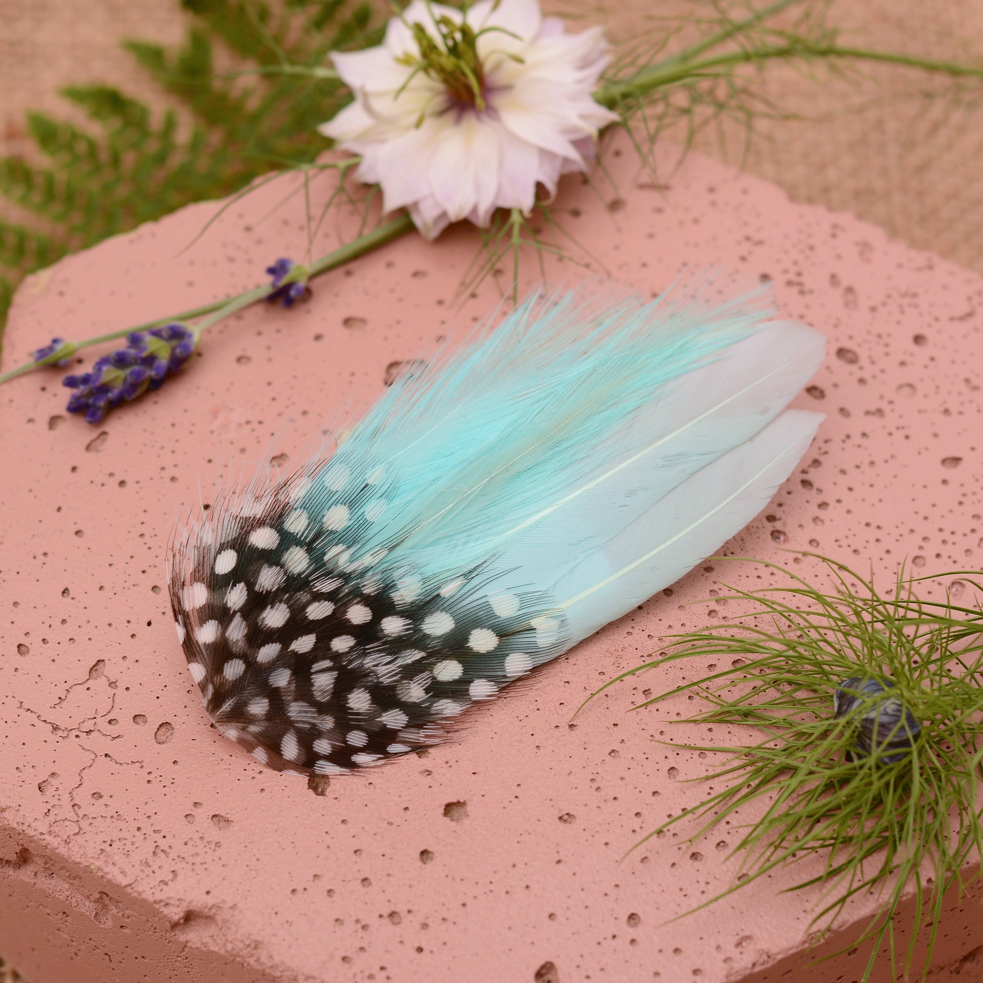 Mint green feather hair clip on a pink stone with flowers and plants around