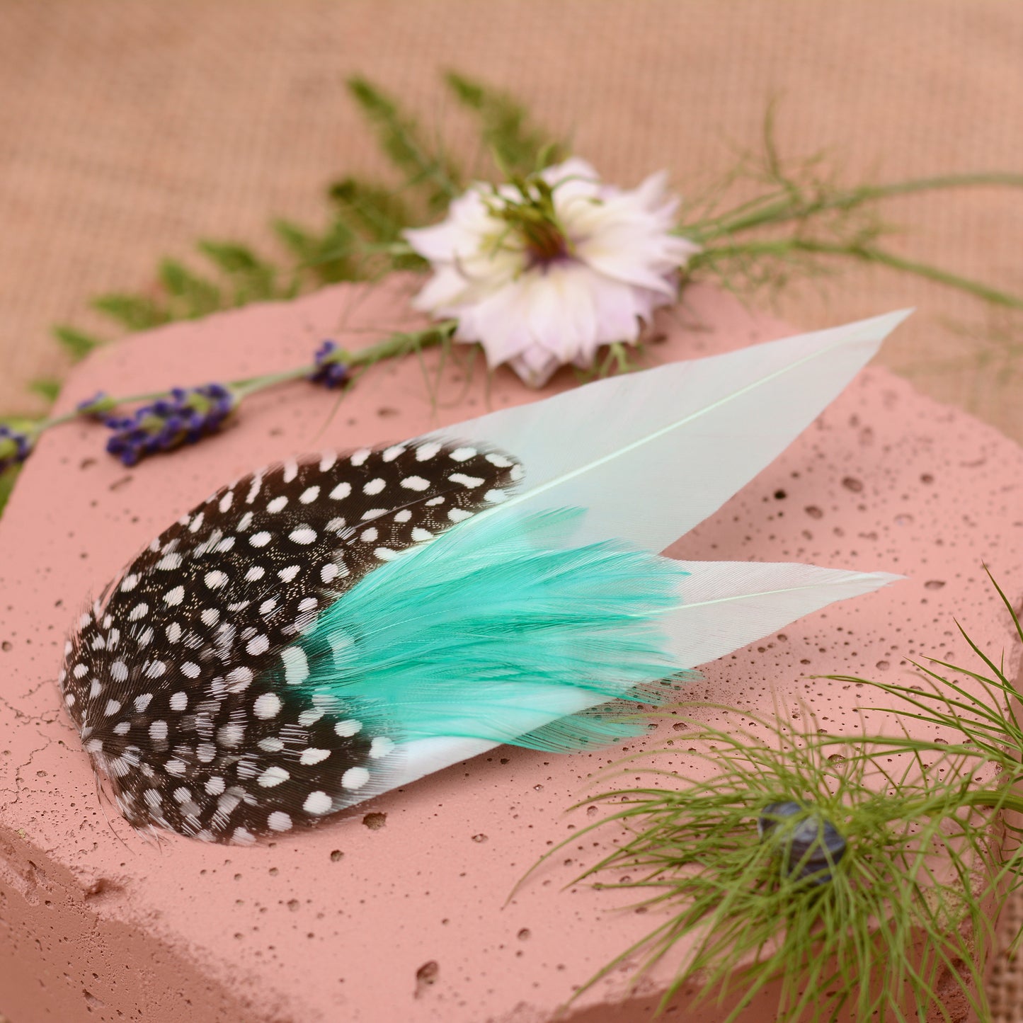 Mint green feather hair clip on a pink stone with flowers and plants around