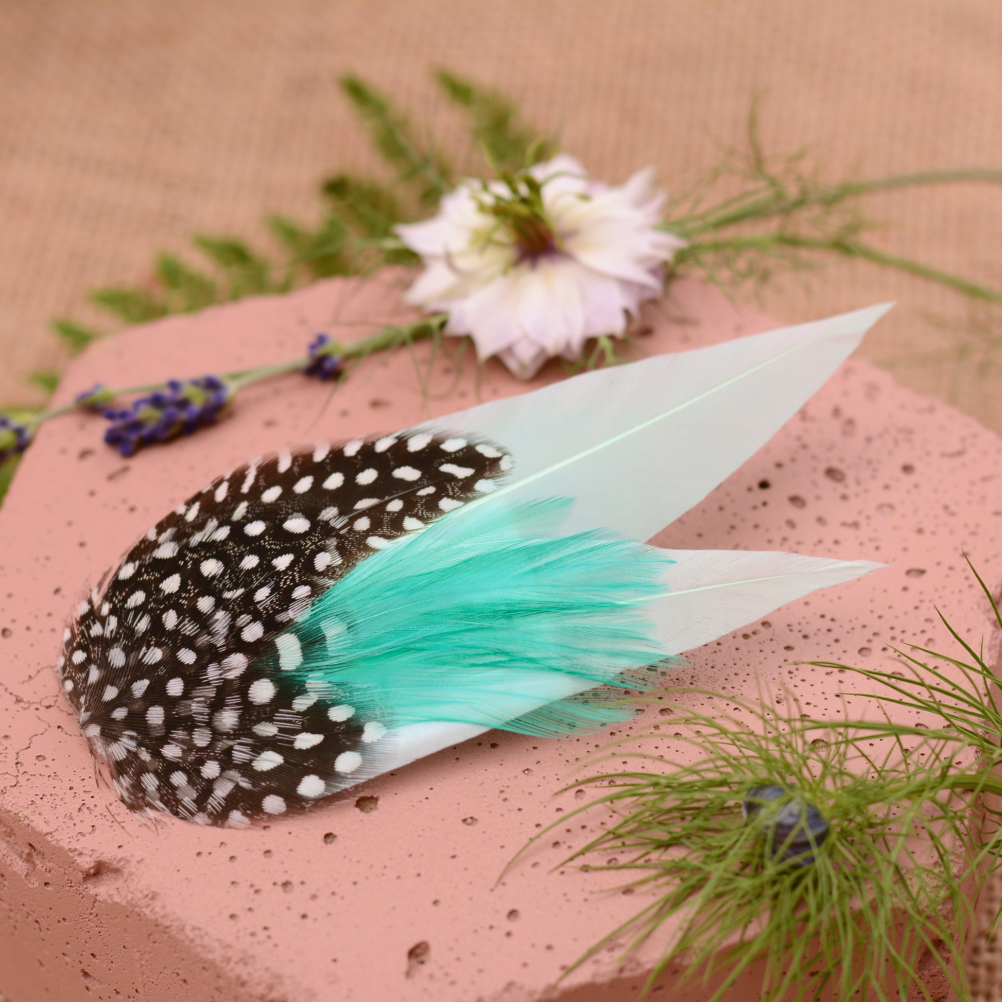 Mint green feather hair clip on a pink stone with flowers and plants around