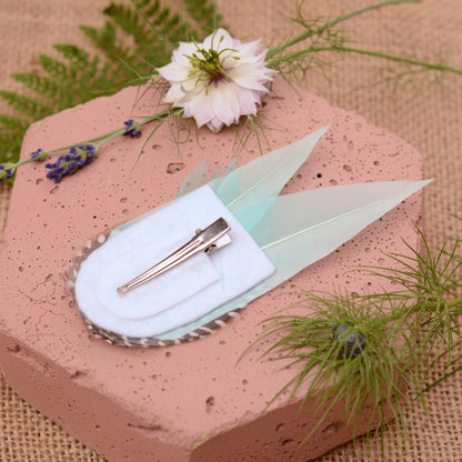 Mint green feather hair clip on a pink stone with flowers and plants around
