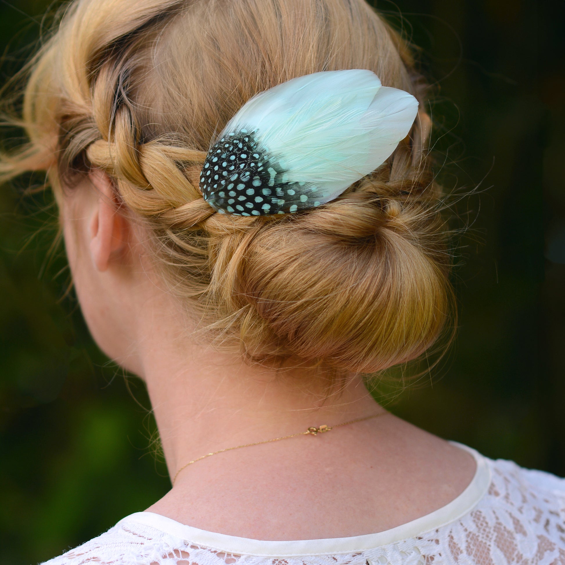 Person with braided hair wearing a decorative mint green  and polka dot feather hair clip against a blurred green background