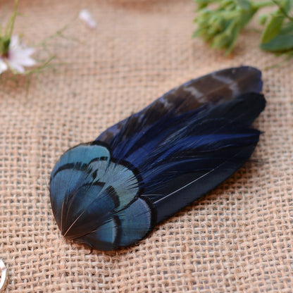 Hair clip crafted in a range of deep blue and black feathers on a textured beige surface with flowers in the background
