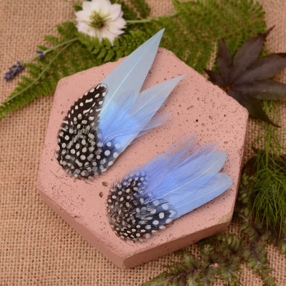 Blue feathered hair clips on a pink surface with flowers and greenery.