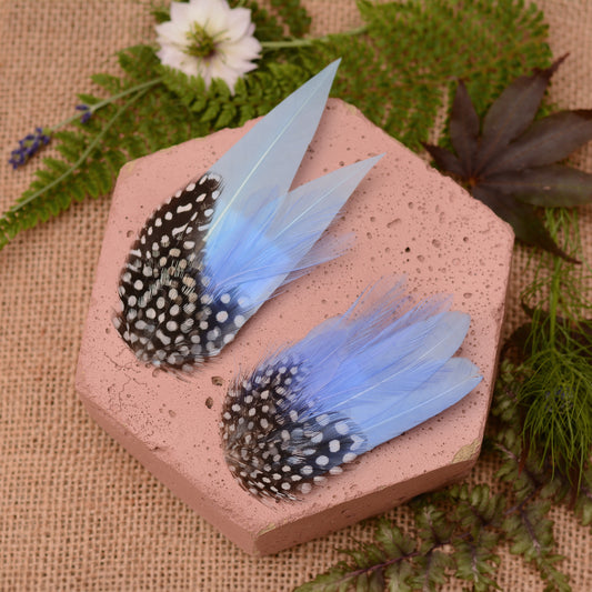 Blue feathered hair clips on a pink surface with flowers and greenery.
