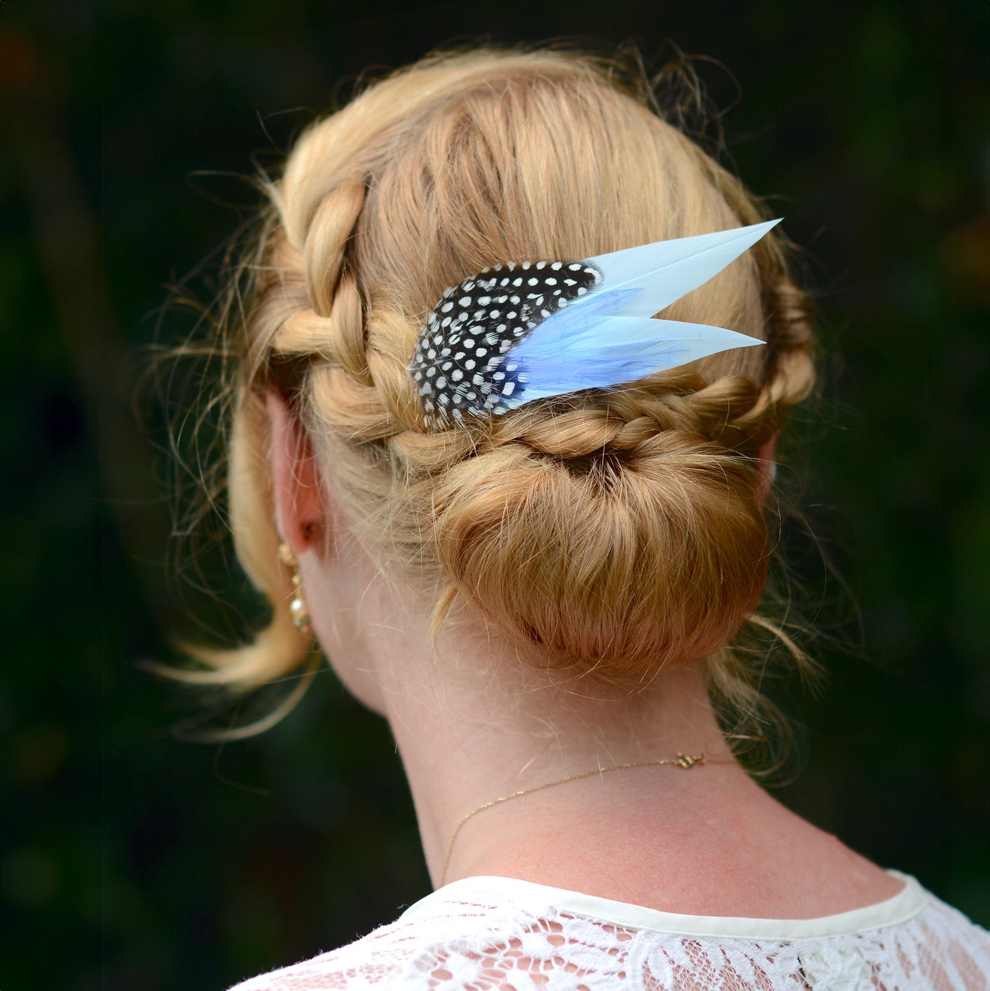 Person with braided hair and blue feather hair accessory against a blurred natural background