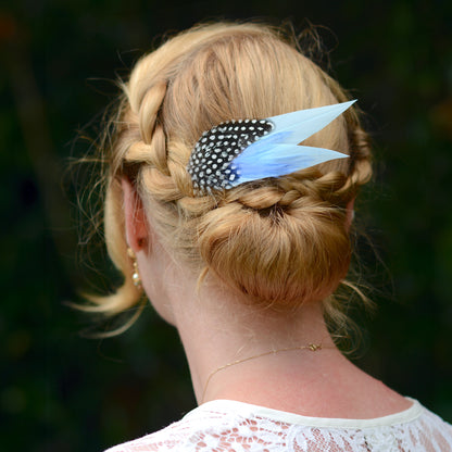 Person with braided hair and blue feather hair accessory against a blurred natural background