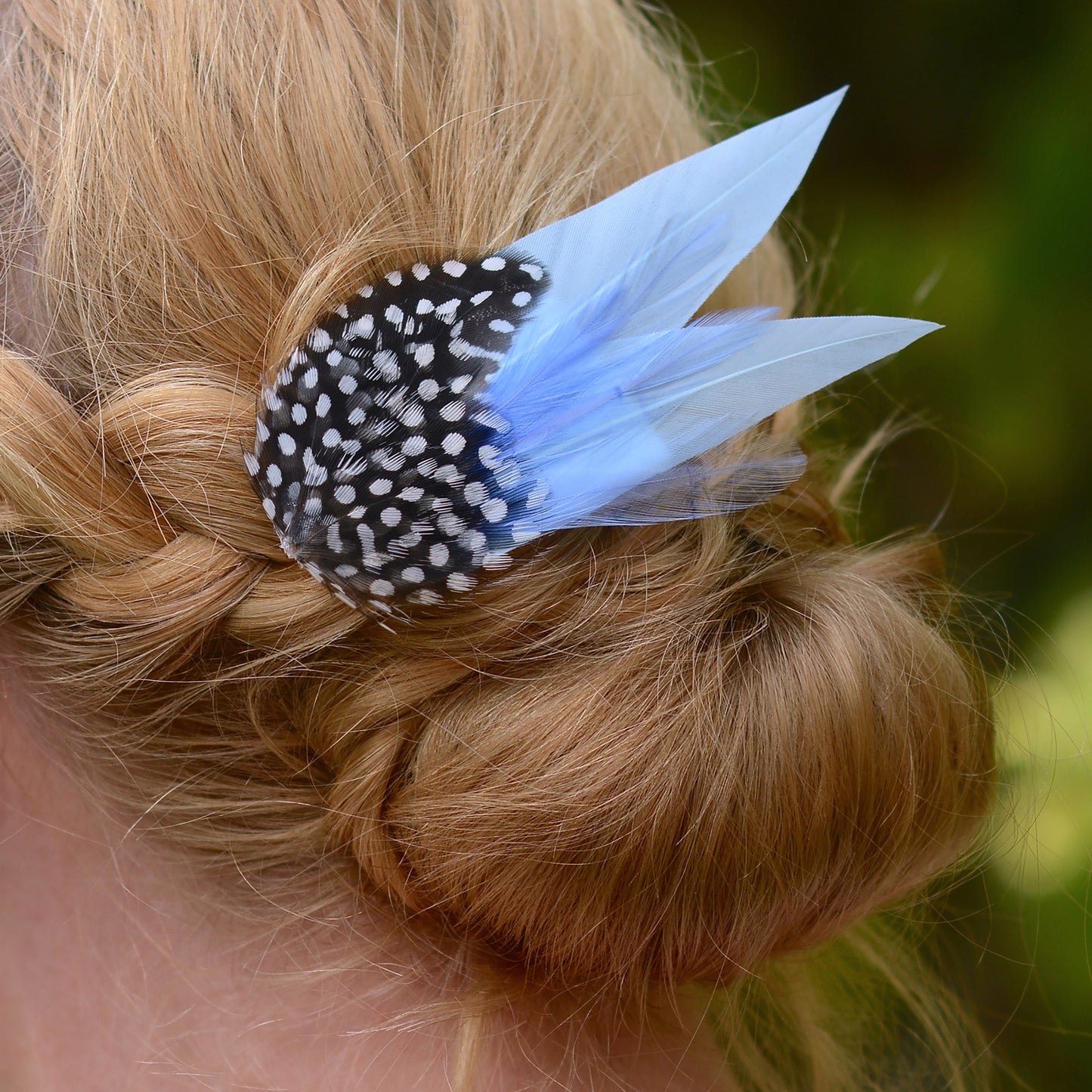 close up of braided hair and blue feather hair accessory against a blurred natural background