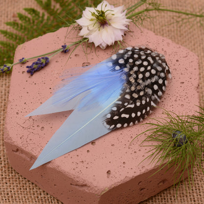 Blue feathered hair clip on a pink surface with flowers and greenery.