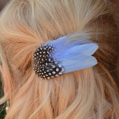 A close-up of a hair accessory clipped into blonde hair, featuring a black and white spotted with light blue feathers.