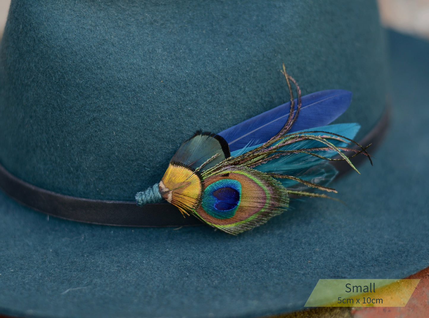 Blue hat with small peacock feather hat pin decoration in teal and navy
