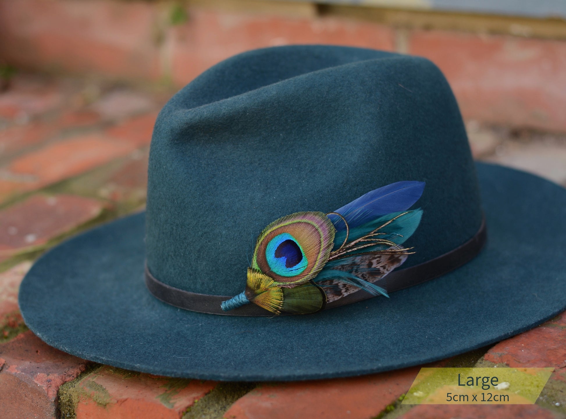 Teal hat with a peacock feather hat pin on a brick surface