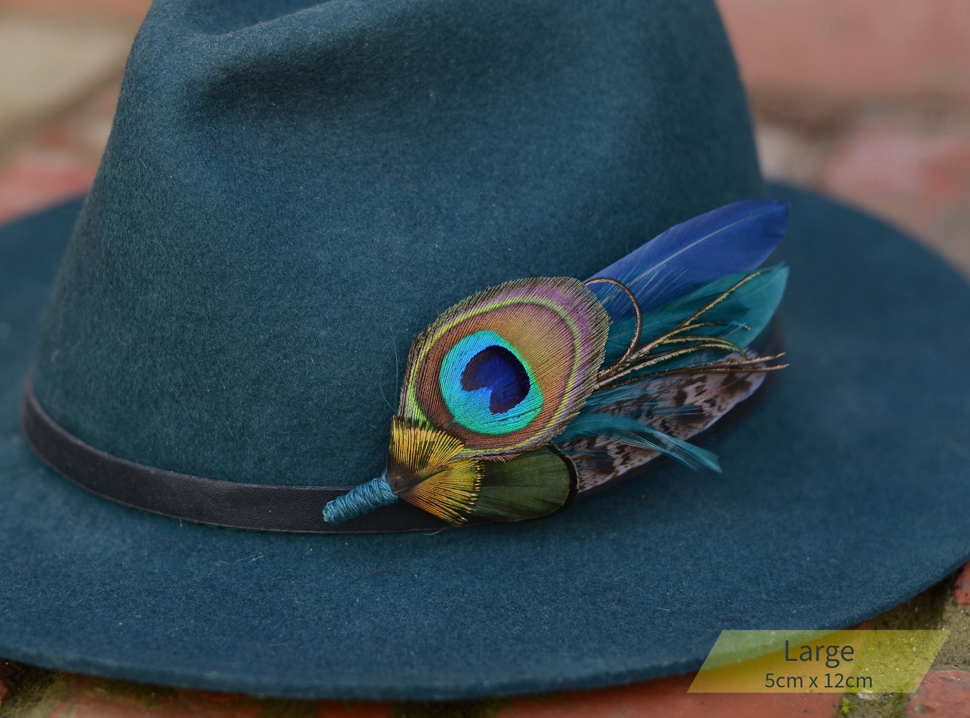 Blue felt hat with peacock feather brooch and a black band on a blurred background