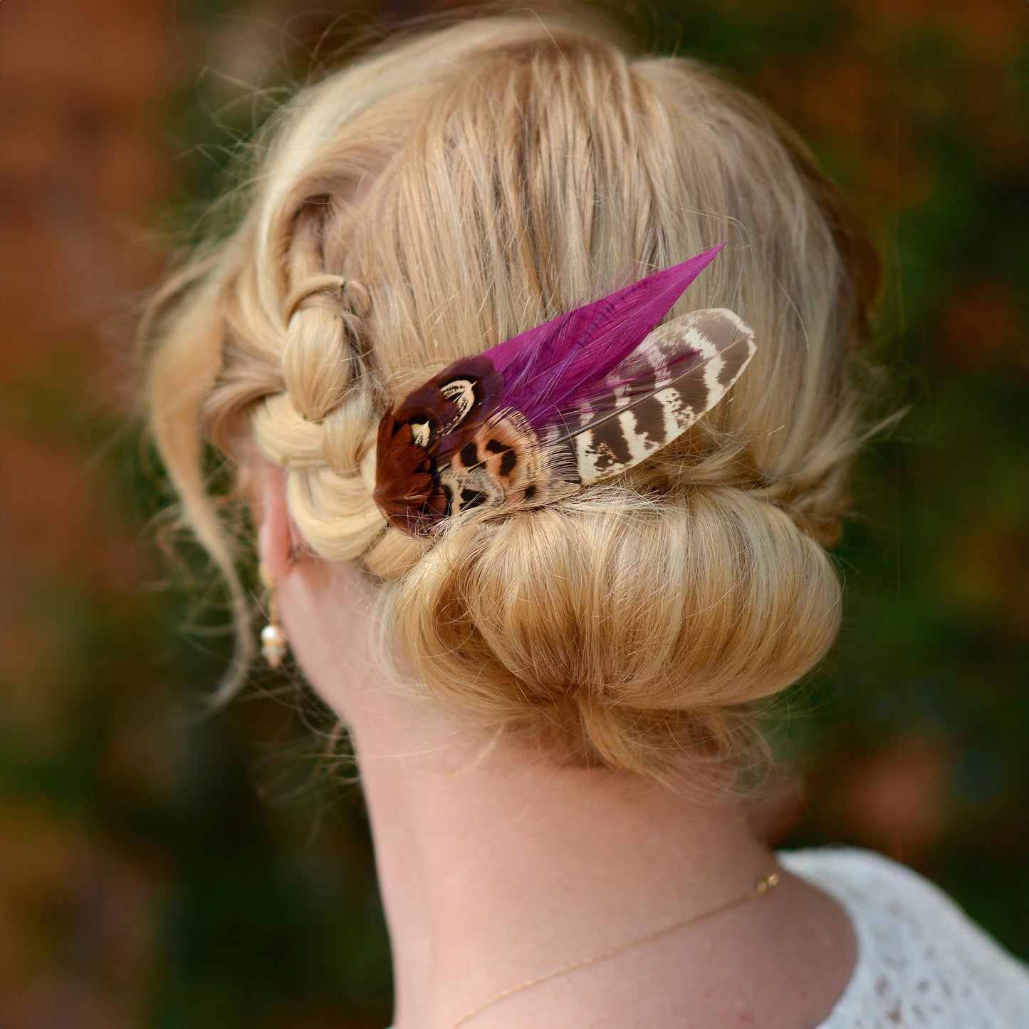 Blonde hair styled in an intricate braid with a decorative pheasant feather accessory.