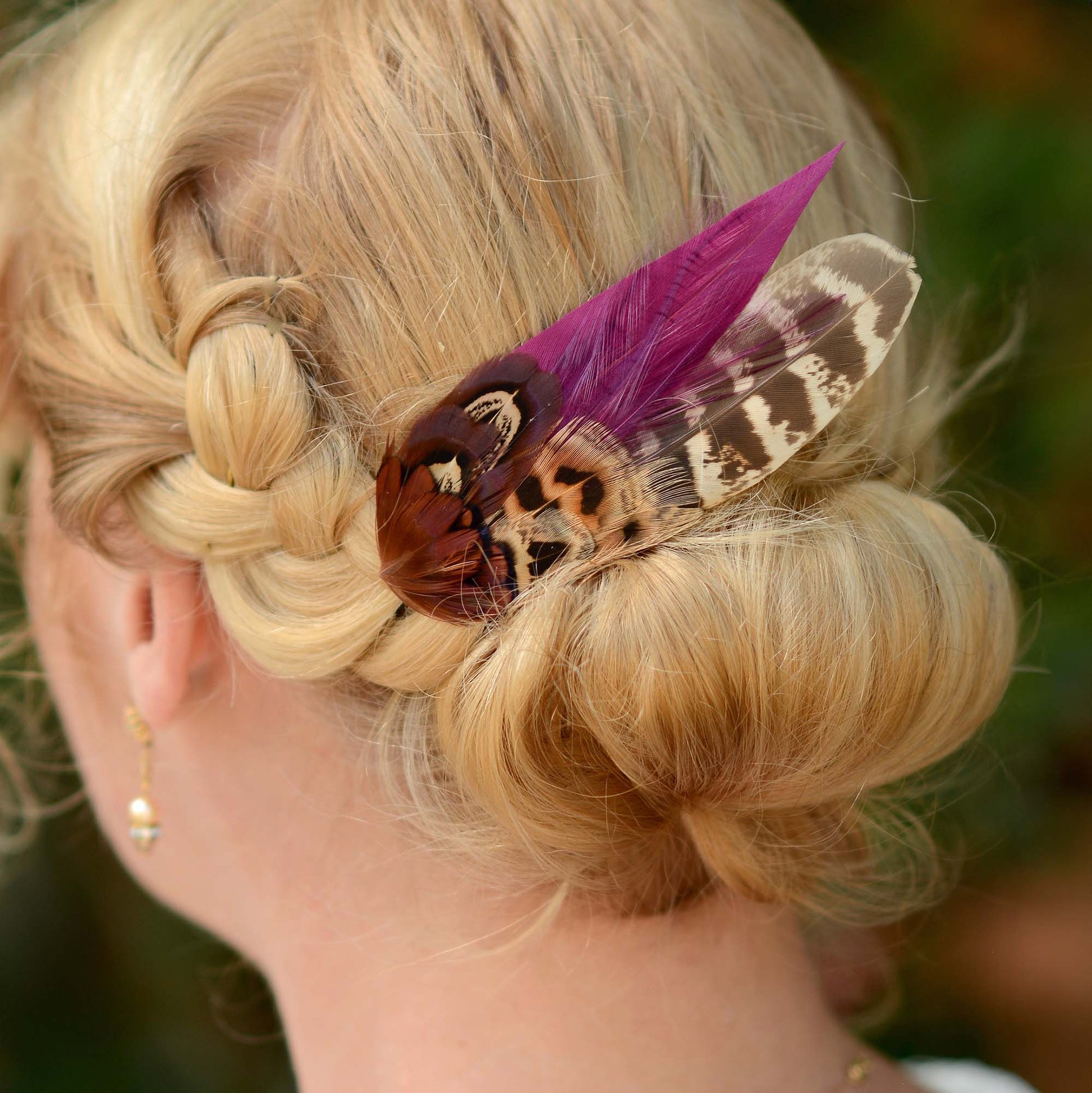 Blonde hair styled in an intricate braid with a decorative pheasant feather accessory.