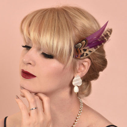 Woman with a feathered hair accessory and pearl necklace against a pink background